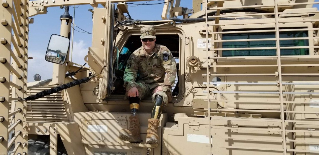Lane sits in the door of a military vehicle during his 2018 return to Afghanistan, bilateral prosthetics and all, proof that he never stopped showing up. Photo courtesy of JP and Crystal Lane
